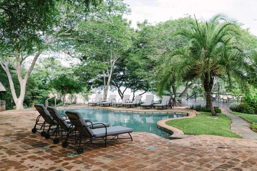 Liegestühle rund um einen Pool mit Palmen im Hintergrund