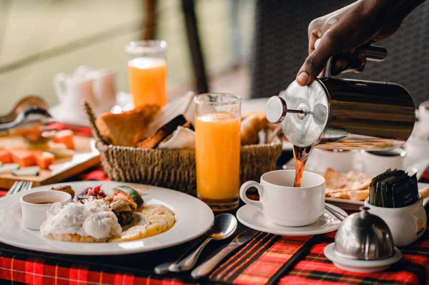 Eine Person gießt Kaffee in eine Tasse auf einem Tisch mit Essen