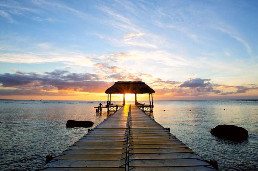 Ein Holzsteg mit einem Strohdach führt ins Meer