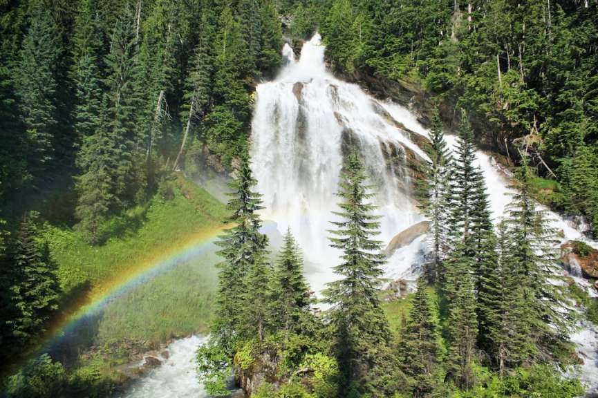 Ein Wasserfall im Wald mit einem Regenbogen davor