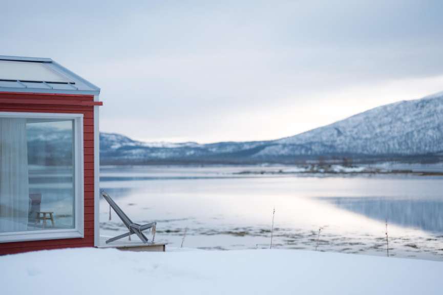 Ein rotes Haus blickt auf einen See mit schneebedeckten Bergen im Hintergrund