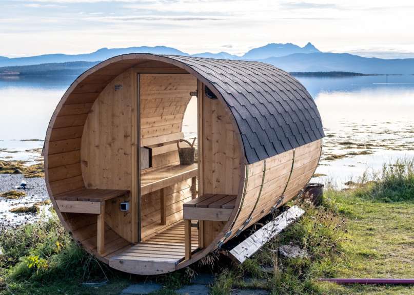 Eine Holzsauna mit einem schwarzen Dach sitzt am Ufer eines Sees