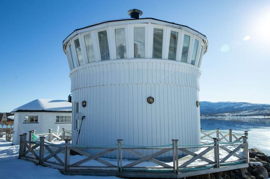 Ein weißer Turm mit vielen Fenstern steht neben einem schneebedeckten See