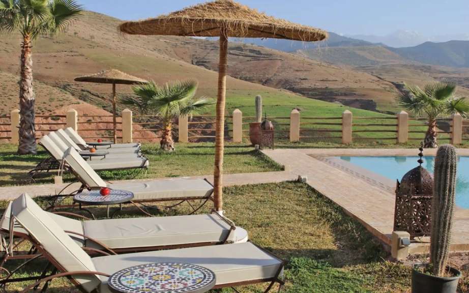 Liegestühle und Sonnenschirme neben einem Pool mit Bergen im Hintergrund