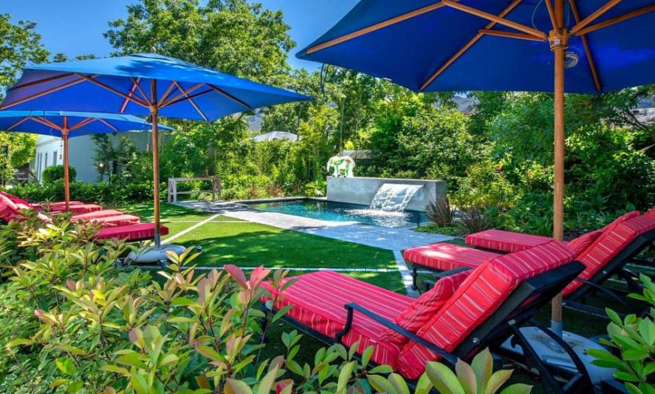 Liegestühle unter blauen Sonnenschirmen neben einem Pool