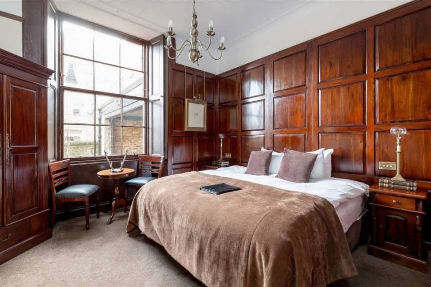Ein Schlafzimmer mit Holzwandverkleidung, einem großen Fenster, einem Bett mit brauner Decke und zwei Nachttischen.