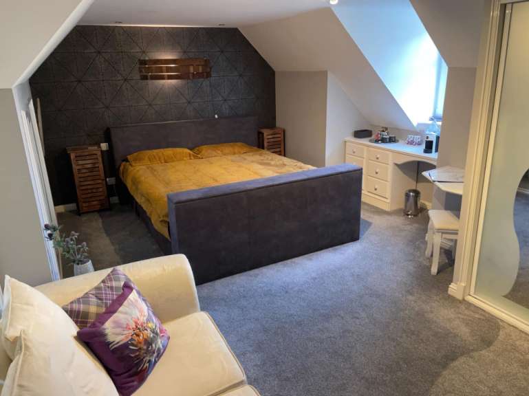 Ein Schlafzimmer mit einem großen Bett, Nachttischen, einem Schreibtisch mit Schubladen und einem Spiegel.