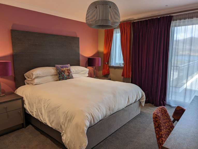 Ein geräumiges Schlafzimmer mit einem großen Bett, einem Nachttisch und einem Schreibtisch mit Stuhl ist zu sehen.