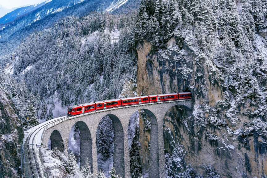 Ein roter Zug fährt über eine Brücke in den Bergen
