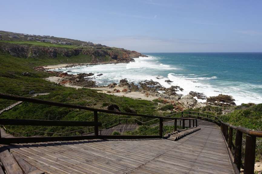 Eine Holztreppe führt hinunter zu einem felsigen Strand
