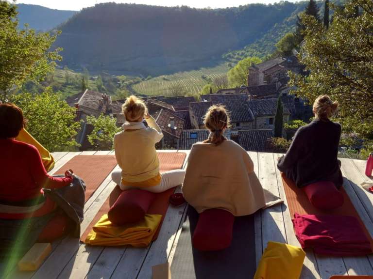 Eine Gruppe von Menschen sitzt auf Yogamatten auf einem Holzdeck