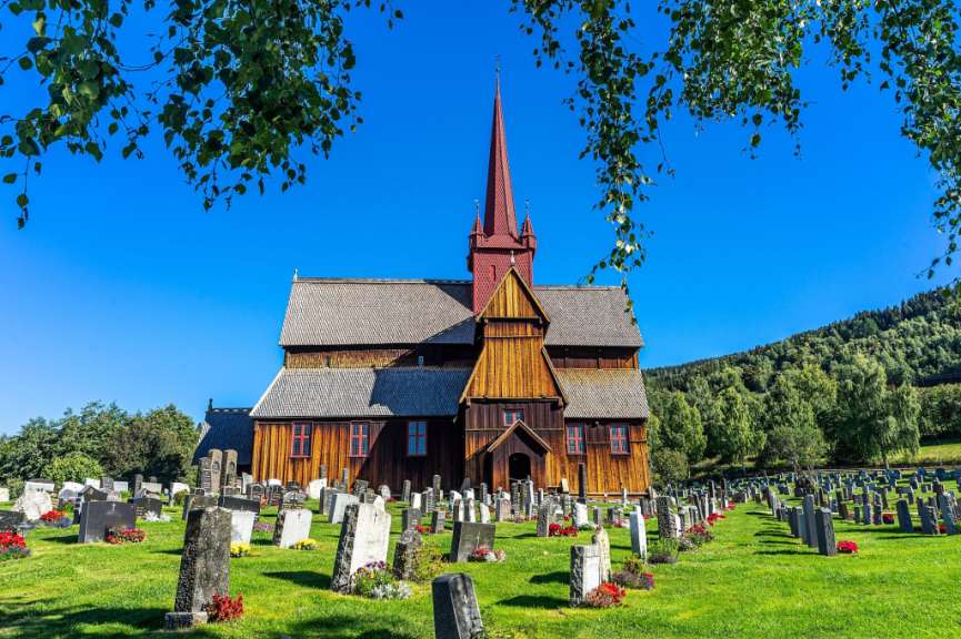 Eine Holzkirche mit einem roten Turm und einem Friedhof davor