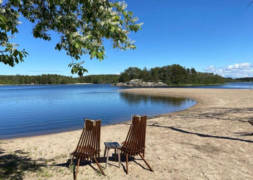 Zwei Holzstühle sitzen an einem Strand mit Blick auf einen See