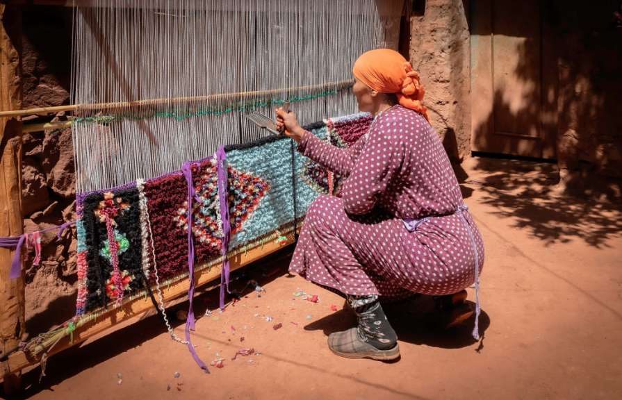 Eine Frau in einem lila Kleid arbeitet an einem Teppich