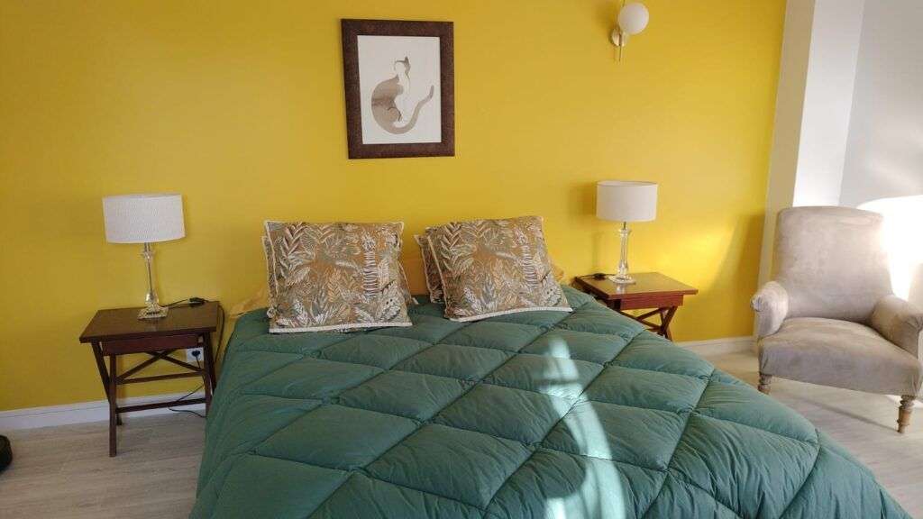 Ein Schlafzimmer mit gelben Wänden, einem Bett mit grüner Decke und einem Sessel.