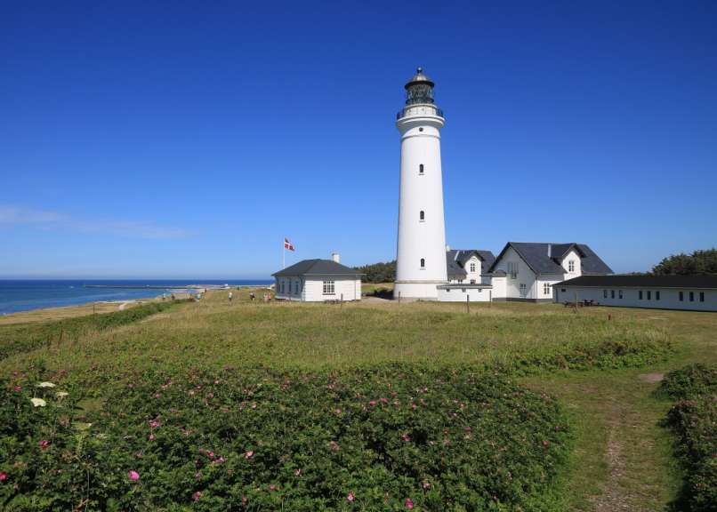 Ein weißer Leuchtturm steht auf einem Hügel mit Blick auf das Meer