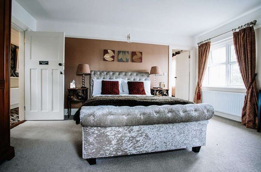 Ein opulent gestaltetes Schlafzimmer mit einem Bett im Chesterfield-Stil und dunklen Nachttischen.