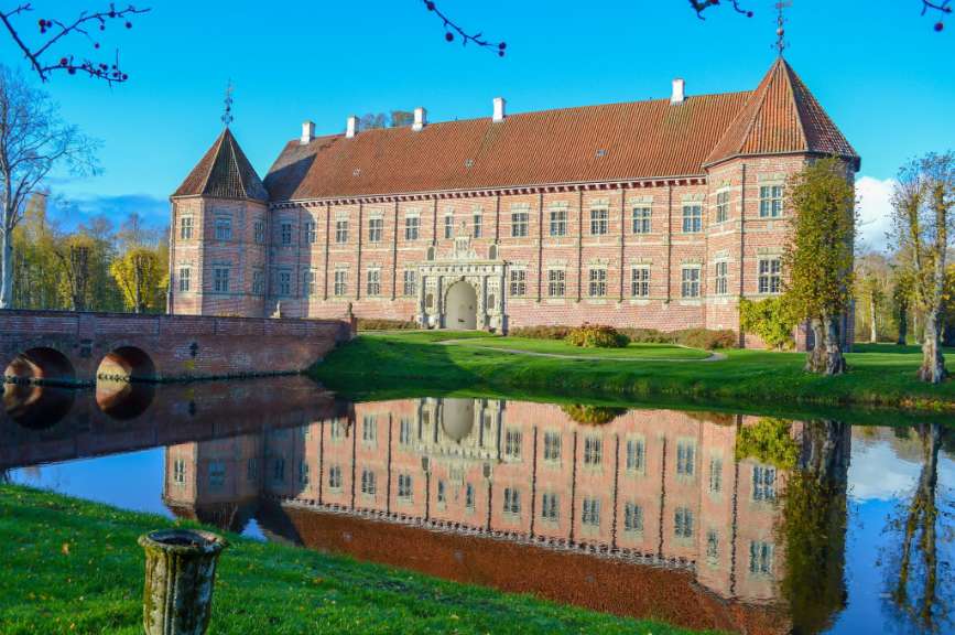 Ein Schloss mit roten Ziegeln wird in einem ruhigen Wasser gespiegelt.