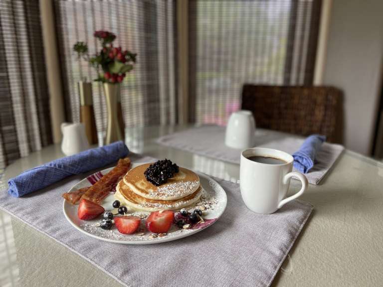 Ein Teller mit Pfannkuchen, Bacon und Beeren neben einer Tasse Kaffee