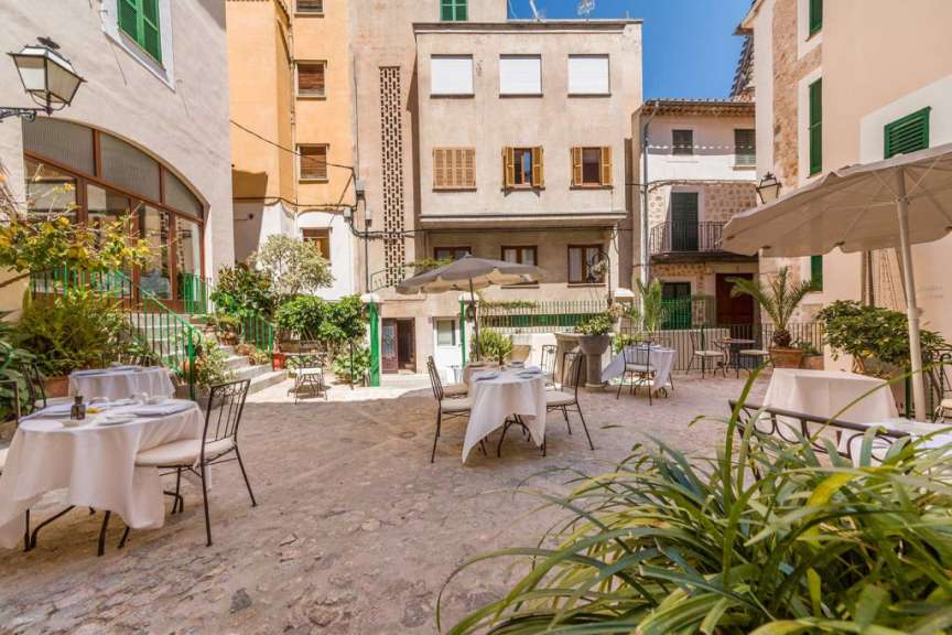 Tische und Stühle stehen in einem kleinen Hof zwischen zwei Gebäuden