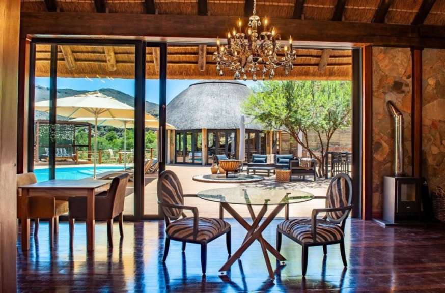 Die überdachte Terrasse eines Luxusresorts öffnet sich zu einem Schwimmbad und einem ummauerten Innenhof mit einem traditionellen Strohdach-Hauptgebäude.