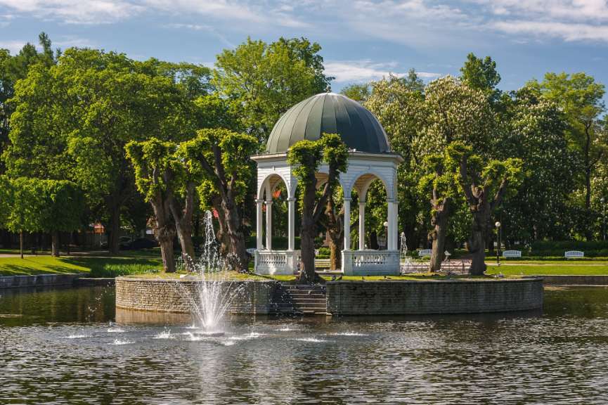 Ein weißer Pavillon mit einer grünen Kuppel steht in einem Park neben einem Teich
