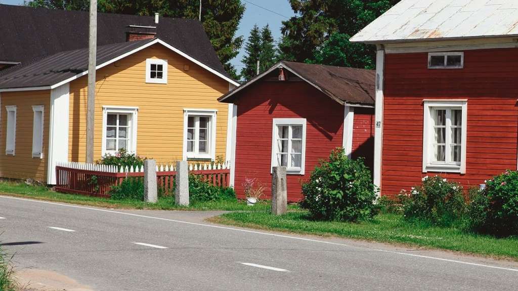 Drei bunte Holzhäuser stehen nebeneinander an einer Straße.