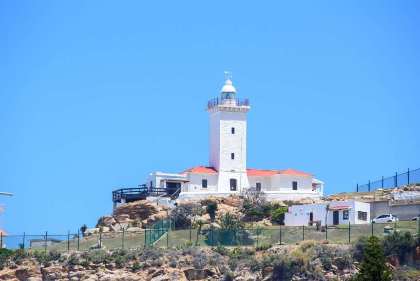Ein weißer Leuchtturm mit rotem Dach sitzt auf einem Hügel