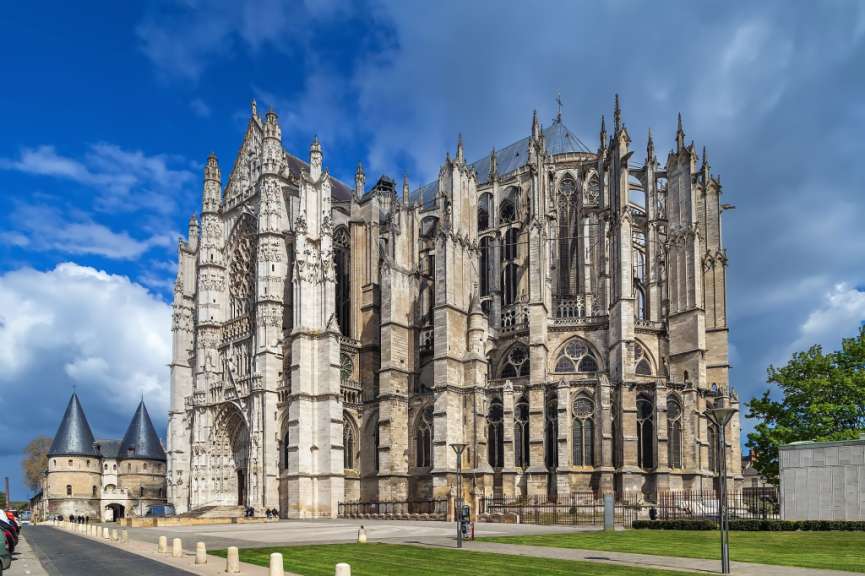 Eine beeindruckende gotische Kathedrale mit vielen Türmchen, Spitzbögen und Verzierungen steht unter einem blauen Himmel mit Wolken.