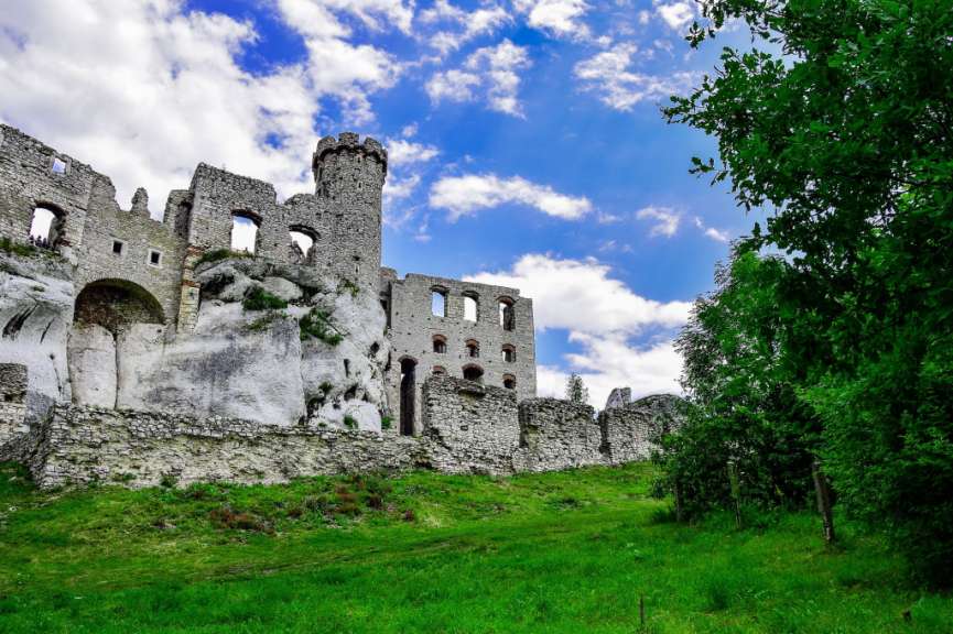 Auf dem Bild sind die Ruinen einer alten Steinburg auf einem felsigen Hügel zu sehen, der mit grünem Gras bedeckt ist, und der Himmel ist mit dramatischen Wolken geschmückt.