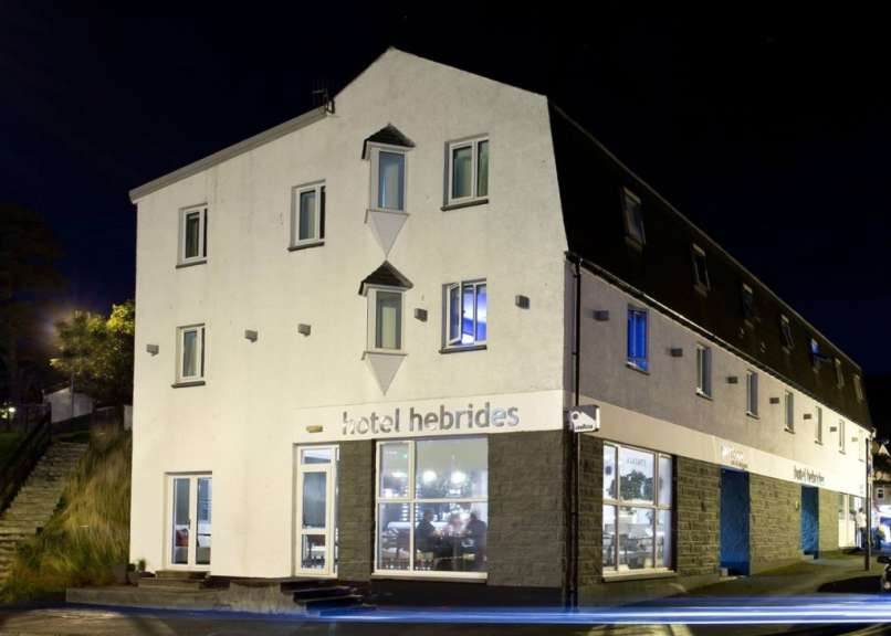 Das Bild zeigt das Hotel Hebrides bei Nacht, mit beleuchteten Fenstern und einem blauen Eingang.