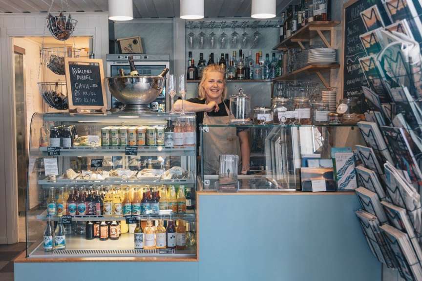 Eine Frau steht hinter einem Schaufenster mit Flaschen und Dosen und einer Auswahl an Getränken