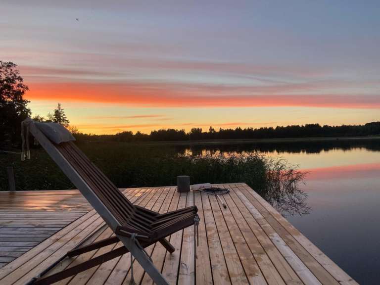 Ein Liegestuhl sitzt auf einem Holzsteg mit Blick auf einen See bei Sonnenuntergang
