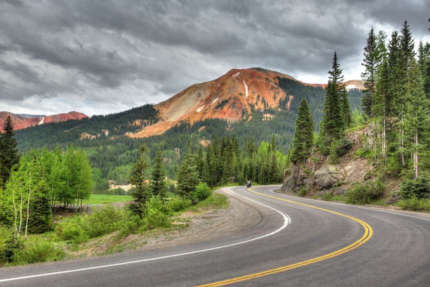 Ein Motorradfahrer fährt auf einer kurvenreichen Straße durch eine bergige Landschaft unter einem dramatischen Himmel.