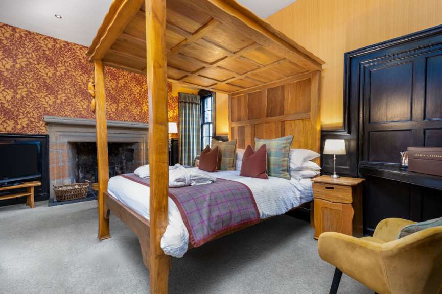 Ein großzügiges Hotelzimmer mit einem Himmelbett aus Holz, einem Kamin und einem bequemen Sessel.