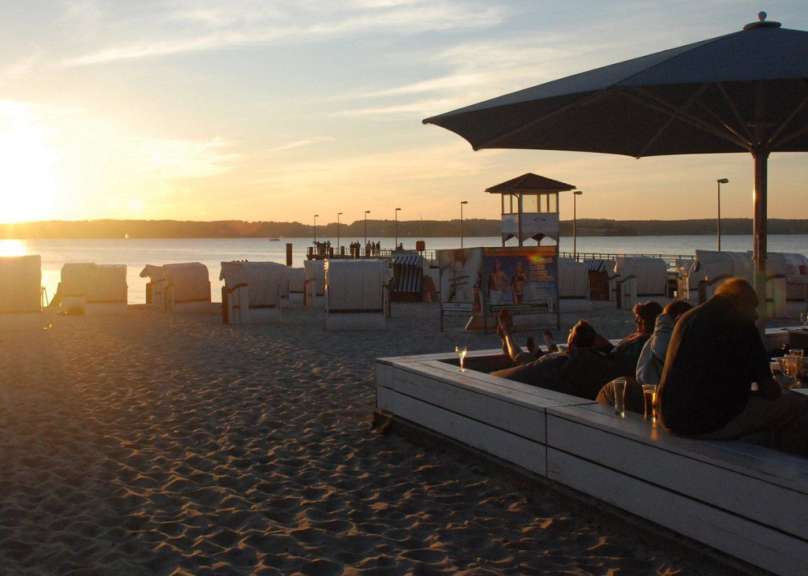 Menschen sitzen auf einer Bank am Strand mit einem Sonnenuntergang im Hintergrund
