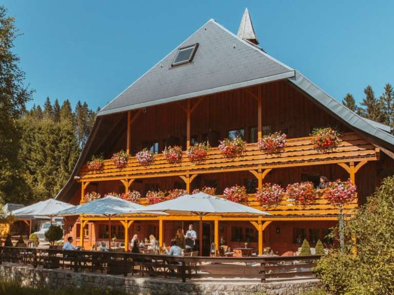 Eine Gruppe von Menschen sitzt auf einer Terrasse vor einem großen Holzhaus