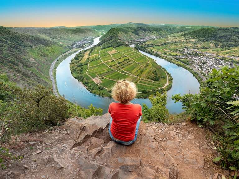 Eine Frau sitzt auf einem Felsen mit Blick auf einen Fluss