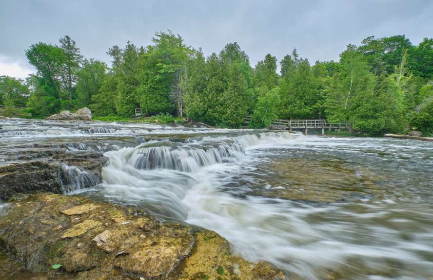 Ein Wasserfall in einem Wald mit einer Holzbrücke im Hintergrund