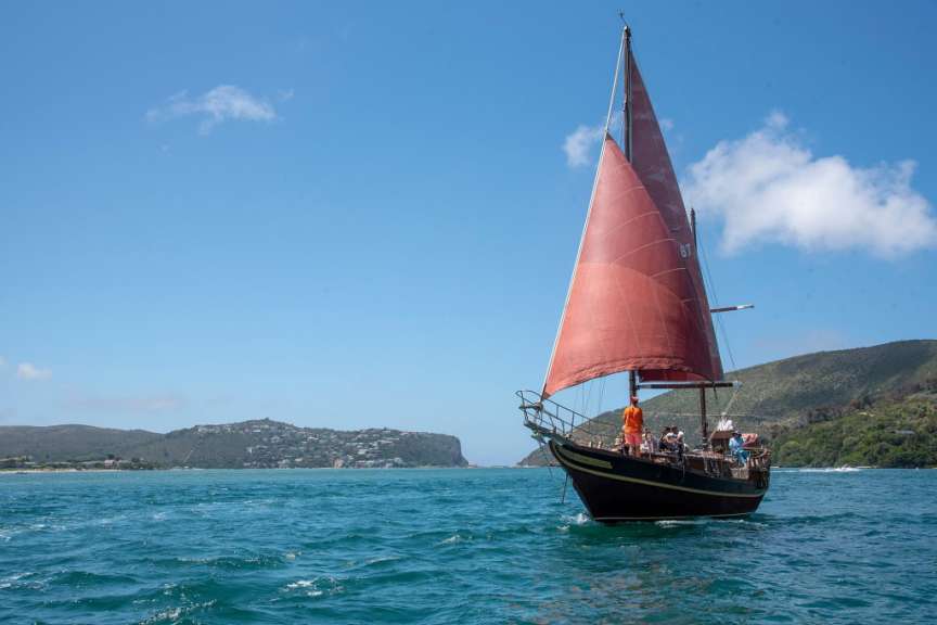 Ein Segelboot mit einem roten Segel fährt durch das Wasser