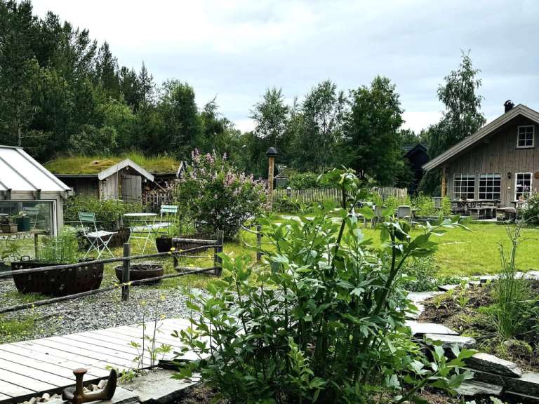 Ein rustikales Haus und zwei kleine Gebäude mit Gründächern sind von üppigem Grün und einem Garten umgeben.