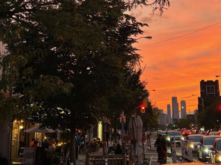 Eine Stadtstraße bei Sonnenuntergang mit vielen Autos und Menschen