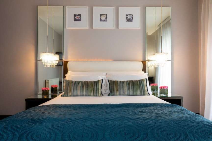 Ein luxuriöses Schlafzimmer mit einem großen Bett, das mit einer blauen Tagesdecke und dekorativen Kissen bedeckt ist, sowie zwei Nachttischen mit Rosen und Spiegeln.