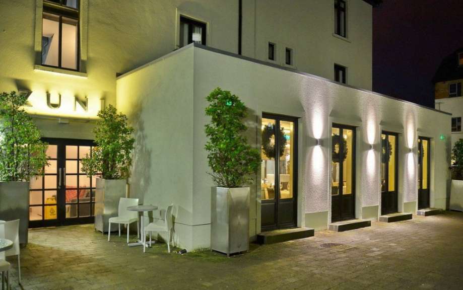 Ein hell beleuchtetes Gebäude mit großen Fenstern und Bäumen vor dem Eingang, aufgenommen bei Nacht.