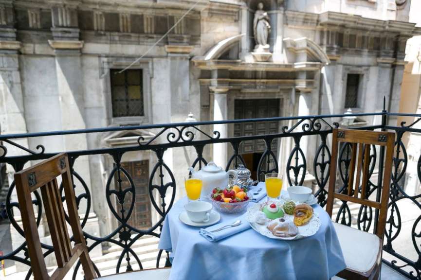 Ein gedeckter Tisch mit Frühstück auf einem Balkon vor einem historischen Gebäude.