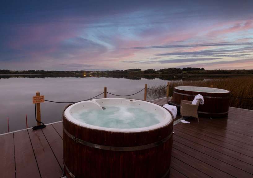 Zwei Whirlpools auf einem Holzdeck neben einem See