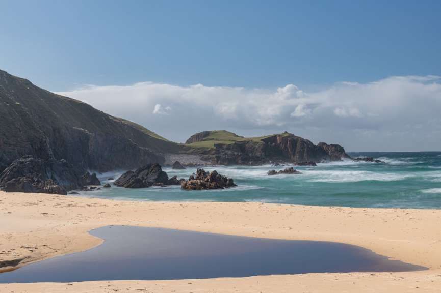 Ein Strand mit einem großen Felsen im Hintergrund