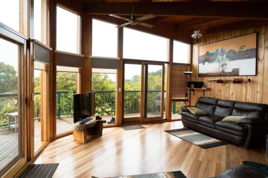 Ein Wohnzimmer mit Holzwänden, bodenlangen Fenstern, einem Ledersofa und einem Fernseher.