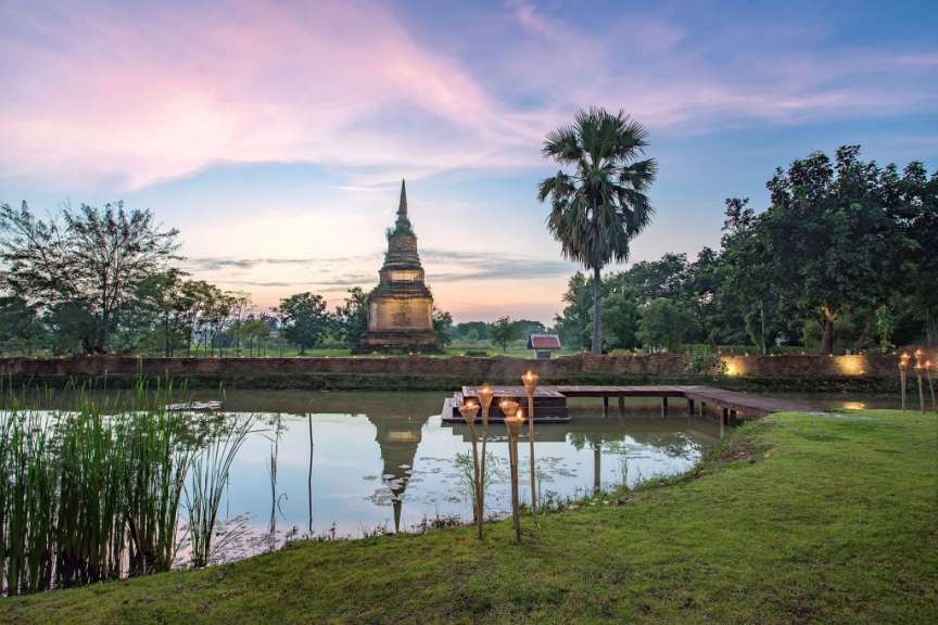 Ein Teich mit Palmen und einem Tempel im Hintergrund