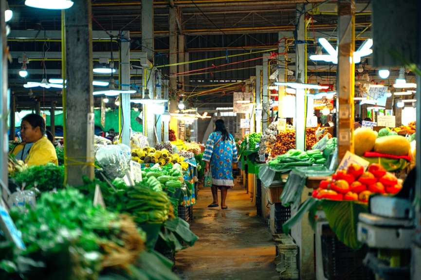 Eine Frau in einem blauen Kleid geht durch einen Obst- und Gemüsemarkt